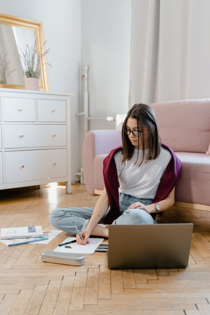 Woman studying with computer and notes on the floor of her apartment.